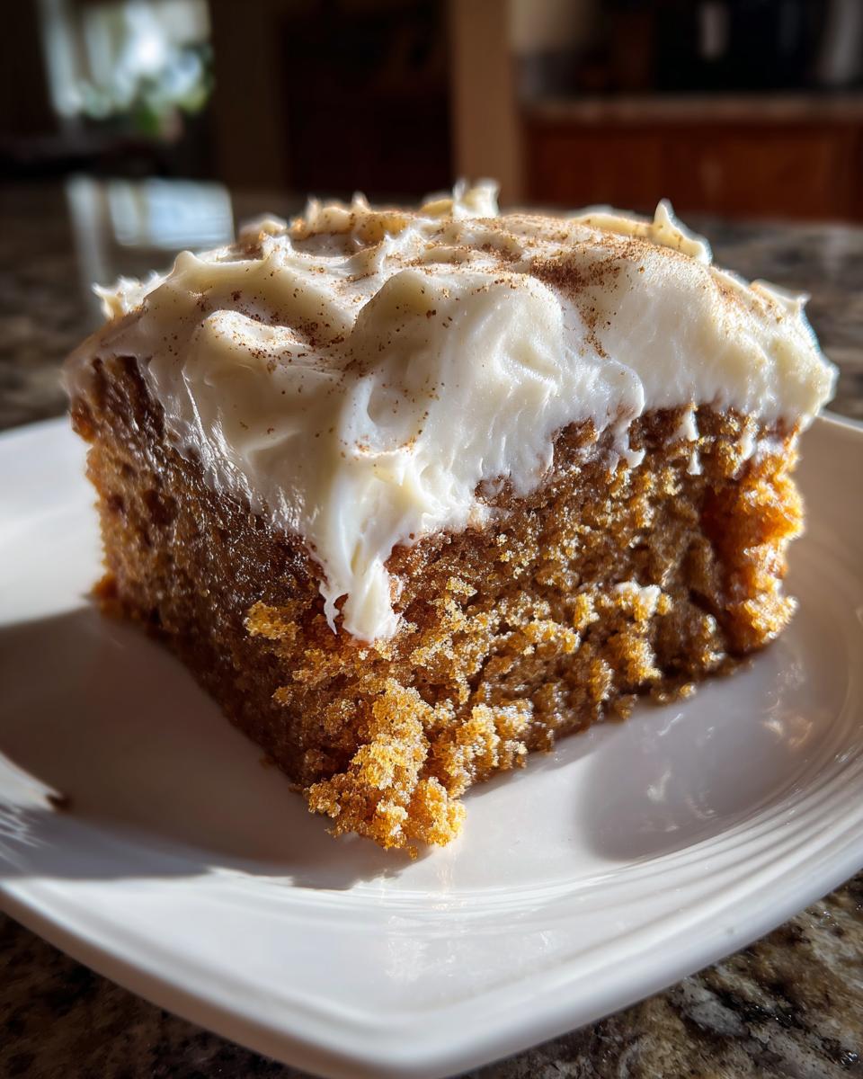 A moist slice of applesauce cake topped with thick cream cheese frosting and a sprinkle of cinnamon.