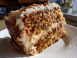 Close-up of a moist slice of applesauce cake layered with thick cream cheese frosting, dusted with cinnamon.