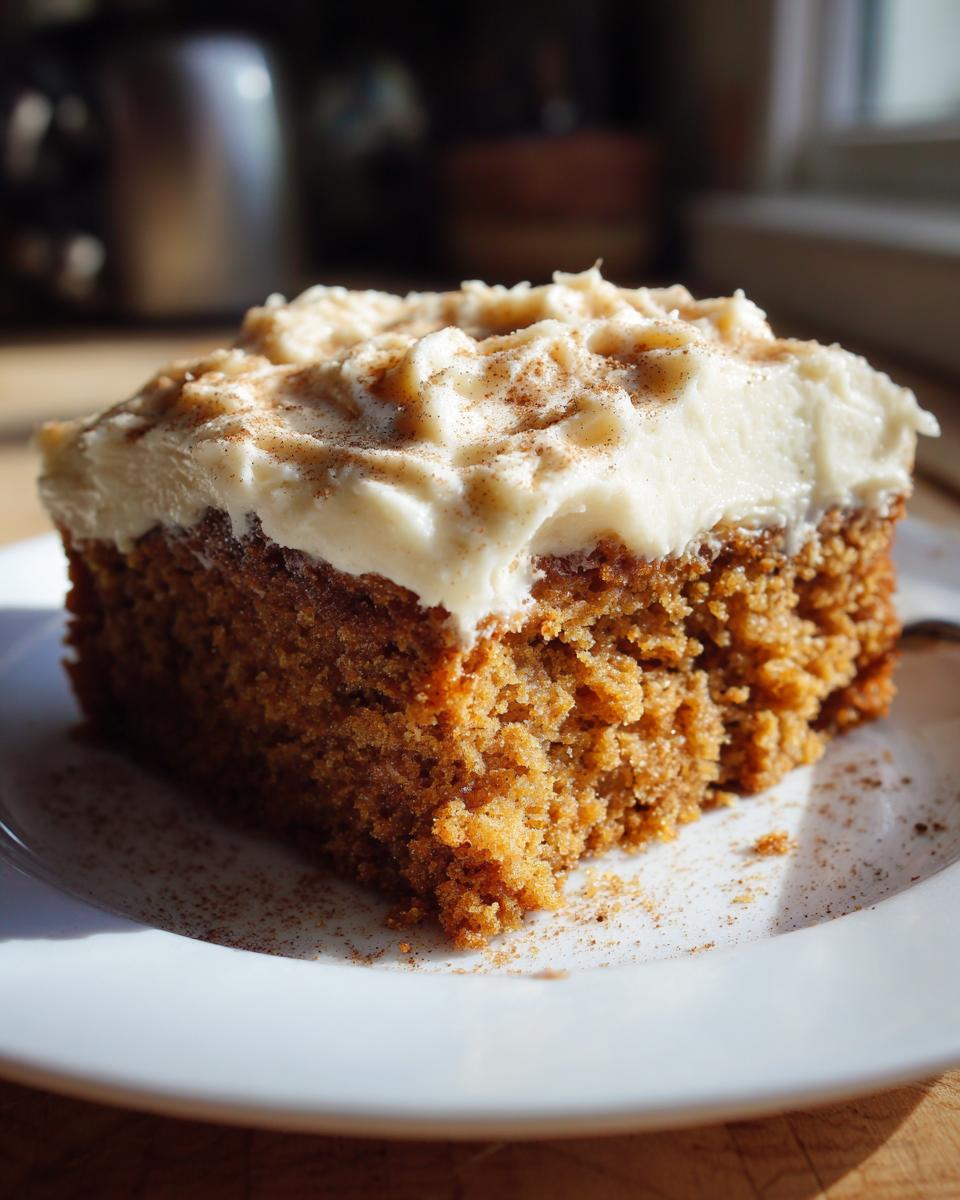 Close-up of a moist slice of applesauce cake topped with thick cream cheese frosting and cinnamon.