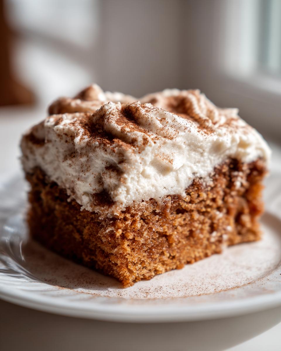 Close-up of a moist slice of applesauce cake topped with thick cream cheese frosting and a dusting of cinnamon.