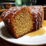 Close-up of a moist slice of bacardi rum cake, drizzled with white icing and sitting in a pool of rum sauce.