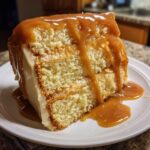 Close-up of a moist slice of two-layer caramel cake covered in thick, dripping caramel sauce.