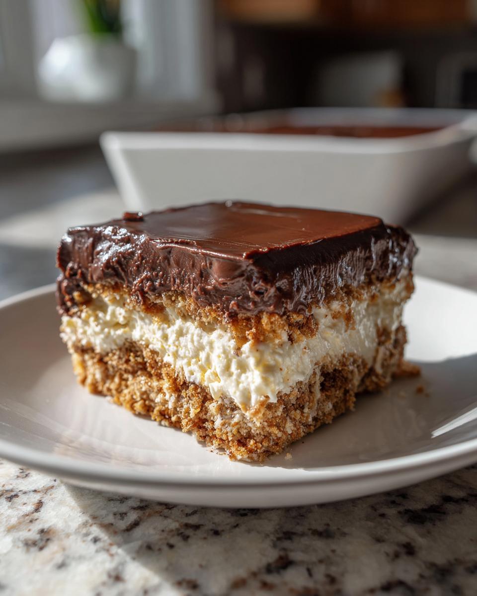 A square slice of no-bake eclair cake showing distinct layers: a graham cracker crust, creamy filling, and rich chocolate frosting.