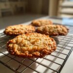 Close-up of golden brown oatmeal lace cookies cooling on a wire rack in bright sunlight.