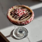 A festive peppermint espresso martini topped with chocolate drizzle and crushed candy canes, served in a coupe glass.