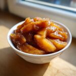 Close-up of rich, caramelized apple pie filling seasoned with cinnamon in a small white bowl.