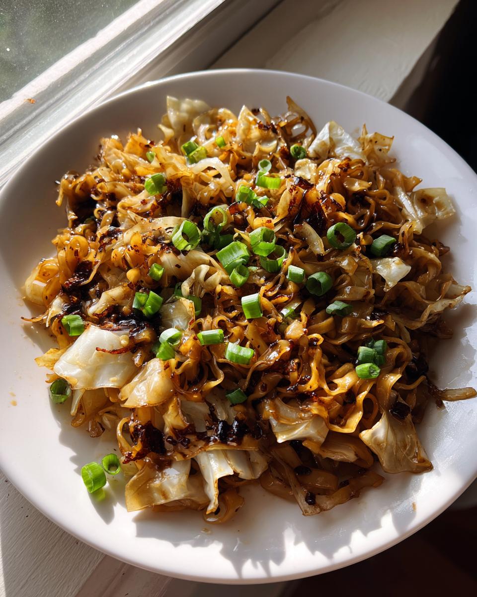 A close-up of quick fried noodles mixed with sautéed cabbage and topped with fresh green onions.