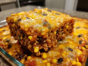 Close-up of a serving slice lifted from a baked Mexican rice casserole topped with melted cheddar cheese, corn, and black beans.