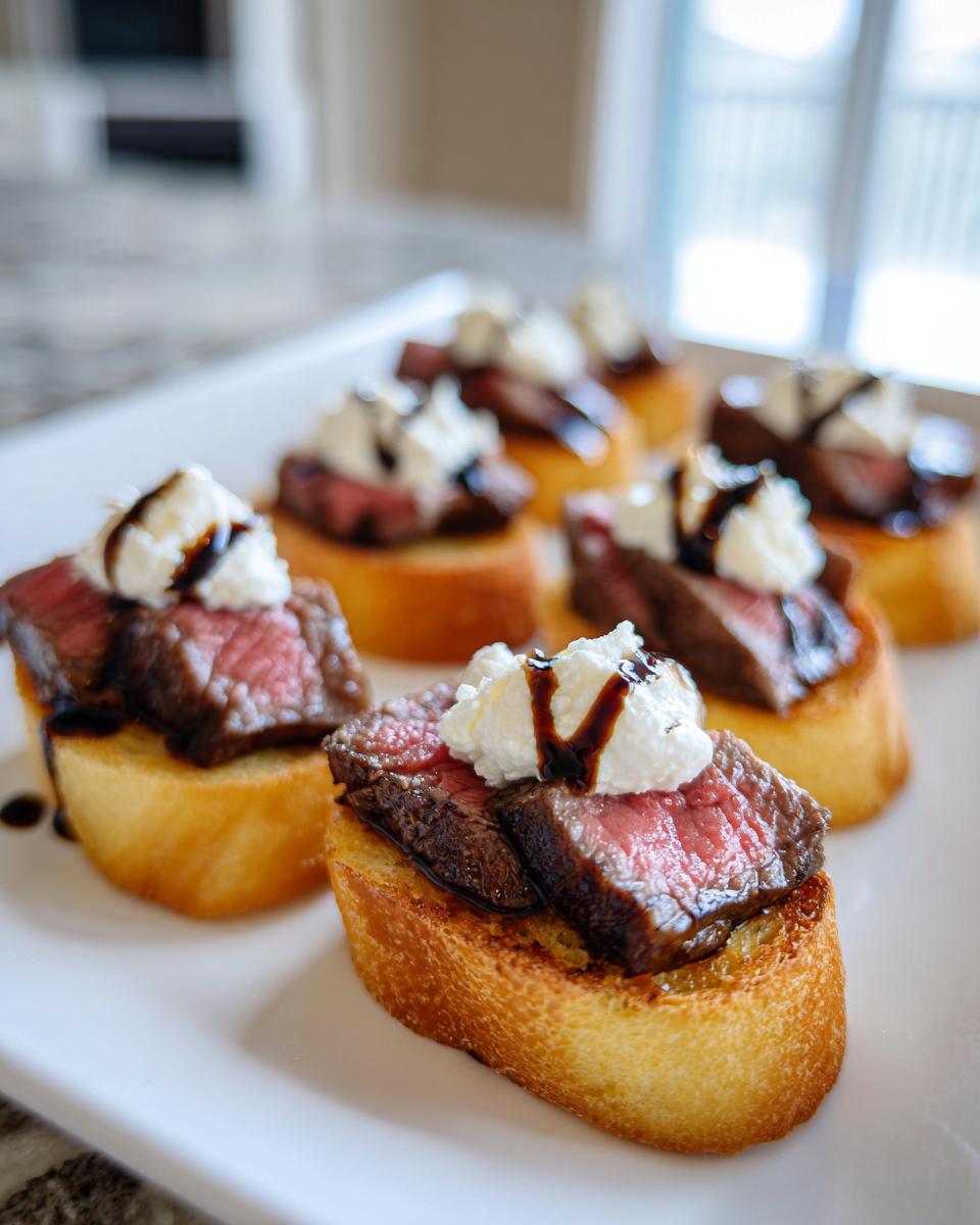 Close-up of several steak crostini bites topped with medium-rare steak, white cheese, and balsamic glaze.