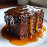 Close-up of a rich, dark square of sticky toffee pudding recipe drenched in thick, glossy toffee sauce.