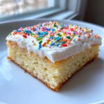 A square slice of soft sugar cookie bars topped with thick white frosting and colorful rainbow sprinkles.