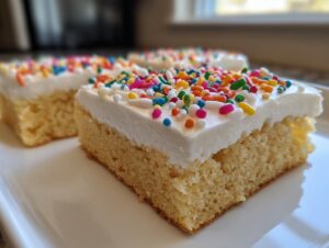 A close-up of a thick slice of soft sugar cookie bars topped with white frosting and colorful sprinkles.
