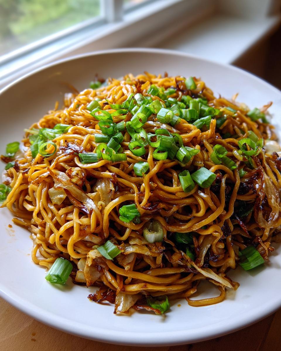 A close-up serving of glossy, brown fried noodles topped generously with bright green chopped scallions.