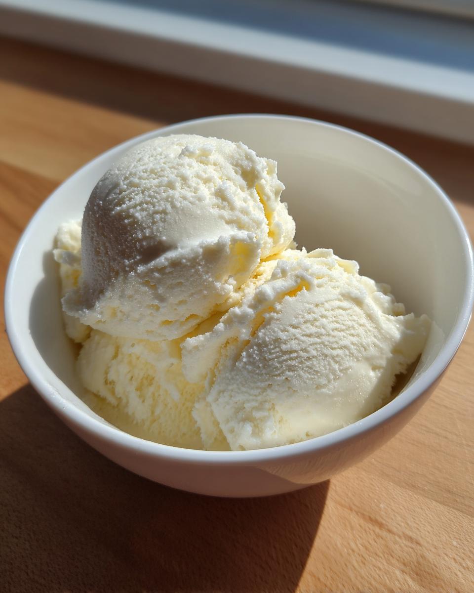 Three scoops of creamy vanilla protein ice cream served in a white bowl, illuminated by bright sunlight.