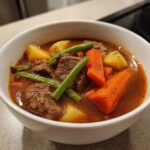 Close-up of a hearty vegetable beef soup featuring chunks of beef, bright orange carrots, green beans, and potatoes in a rich broth.