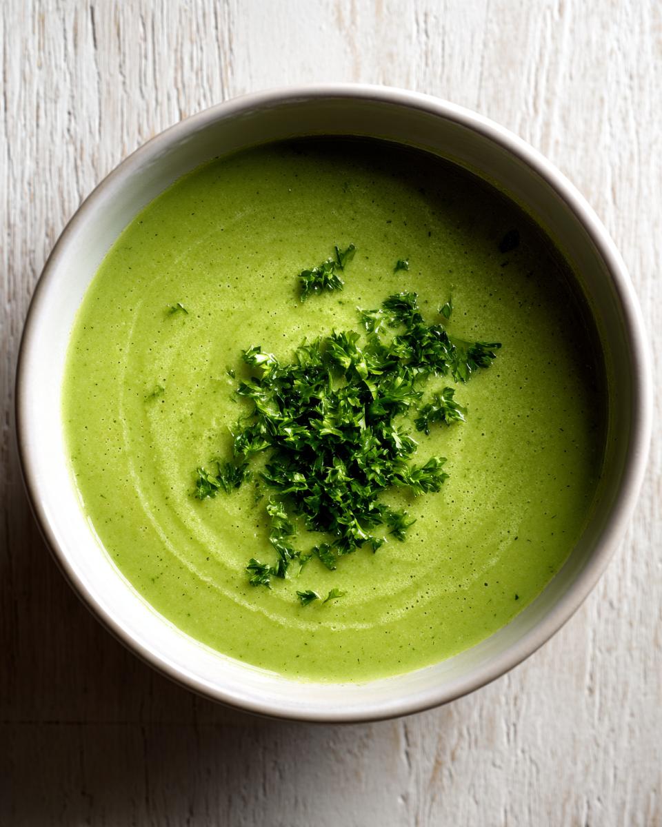Overhead view of a bowl of bright green zucchini soup garnished with fresh chopped parsley.