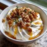 A close-up of creamy whipped ricotta dip topped generously with walnuts, honey drizzle, and fresh thyme sprigs.