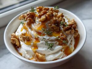 Close-up of a bowl of creamy whipped ricotta dip topped generously with candied walnuts, honey drizzle, and fresh thyme sprigs.